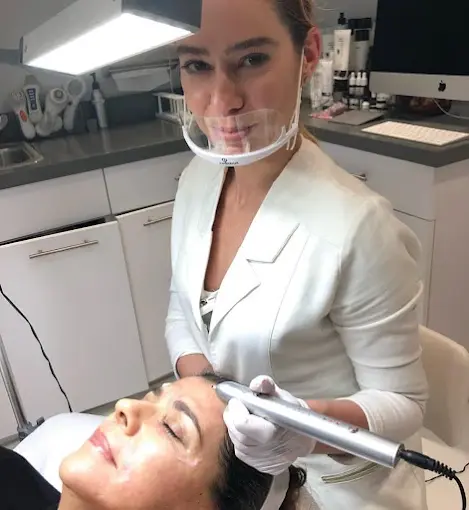 A skincare professional performing a facial treatment with a handheld aesthetic device on a female client in a modern beauty clinic.
